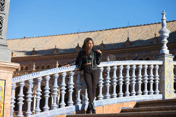 stock image young and beautiful black latin woman is travel in spain and visits the most important square in the city of seville. The woman is dressed in modern and casual black clothes.