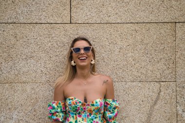 Young beautiful blonde woman with sunglasses leaning against a brown wall in different postures and gestures, happy, sad, depressed, hateful, tired. Concept expressions