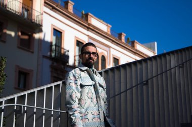 Portrait of young handsome gay man with beard and glasses. The man is dressed casually and in modern clothes and is serious and angry.