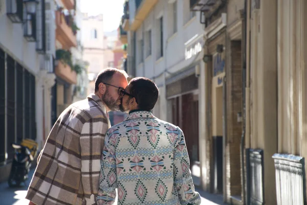 一对年轻的男同性恋夫妇带着手提箱走在街上 这对夫妇去旅行 照片是从后面拍的 他们在接吻 度假和旅行概念 — 图库照片
