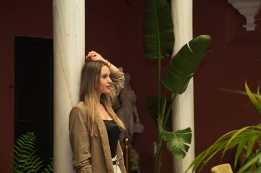 Young and beautiful blonde Latin woman is leaning against a marble column in the inner courtyard of a hotel. The woman is sad and pensive with anguish. Concept depression and stress.