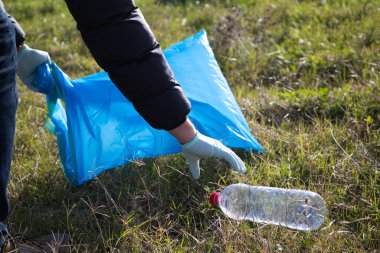 Hand detail of a volunteer collecting plastic bottle from the forest to put in the recycling bag. Concept of Earth Day and World Environment Day June 5.