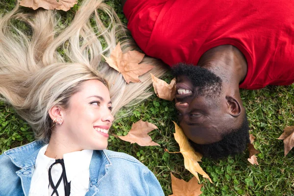 stock image Happy interracial couple lying on the grass. Couple looks at each other with happiness.