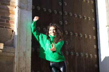 Kıvırcık saçlı, yeşil yün paltolu güzel, genç esmer kadın Seville, İspanya 'da bir binanın girişinde duruyor. Kadın mutlu ve şehirde tatilinin tadını çıkarıyor..