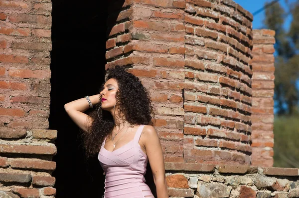 美丽的黑发女人 卷曲的头发在一座废弃的旧建筑的废墟中 这个女人穿着雅致的粉色和窄裙 — 图库照片