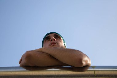 Kot pantolon, beyaz tişört ve yeşil başörtüsü giymiş yakışıklı bir adamın portresi. Genç adam korkuluklara yaslanıyor ve farklı ifadeler takınıyor. Sokak ve modern gençlik kültürü.