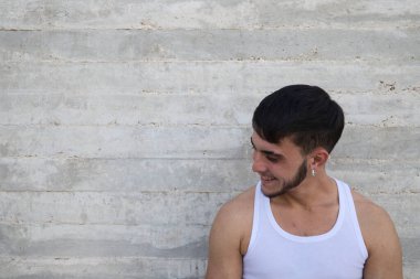 Beyaz tişörtlü genç yakışıklı gri duvarın önünde farklı ifadeler takınıyor. Adam mutlu ve gülümsüyor. Farklı ifadeleri kavra.