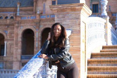 young and beautiful black latin woman visits the most important square in the city of seville. The woman leans her arms on the railing and makes serious and angry expressions.