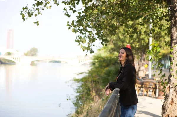 Beautiful young woman leaning over the railing of the river in Seville, Spain. The woman is happy and relaxed looking at the horizon where you can see the other side of the river with the city.