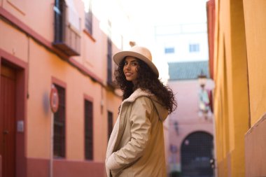 Young and beautiful Hispanic brunette woman with curly hair wearing a hat and coat for the cold walking in the city of seville while making different expressions and having fun.