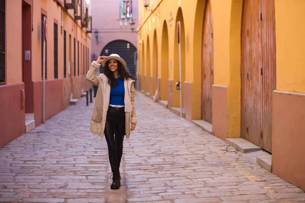 stock image Young and beautiful Hispanic brunette woman with curly hair wearing a hat and coat for the cold walking in the city of seville while making different expressions and having fun.