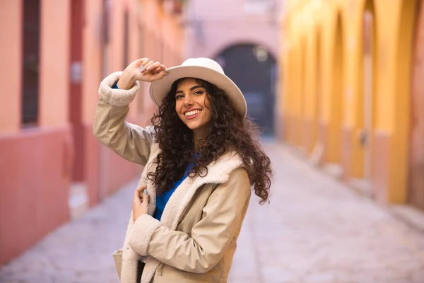 stock image Young and beautiful Hispanic brunette woman with curly hair wearing a hat and coat for the cold walking in the city of seville while making different expressions and having fun.