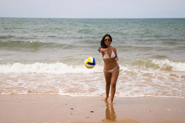 ビーチには 若く美しいラティーナの女性がサングラスをかけています 女性は海岸からカメラにバレーボールを投げつけている 休日や旅行のコンセプト スポーツ — ストック写真