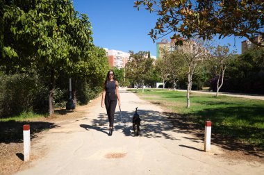 Güzel ve esmer İspanyol kadın bir Doberman köpeği olan köpeğini gezdiriyor. Kadın çok zarif siyah giyinmiş. Evcil hayvanlar ve hayvanlar konsepti.