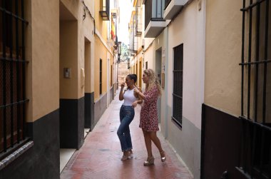 Sevilla 'nın dar sokaklarında gezinen iki güzel kadın. Kadınlar Avrupa 'da tatildeler ve şehrin tarihi merkezini ziyaret ediyorlar..