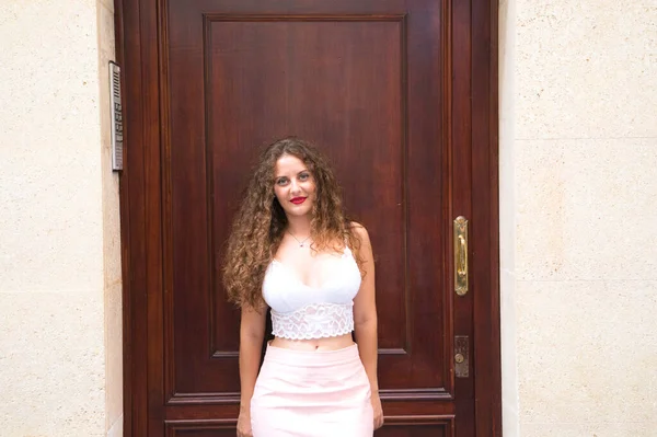 卷发蓝眼睛的女人站在她居住的大楼门口 这个女人穿着一条粉红色的短裙和白色的上衣 — 图库照片