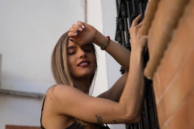 Siyah tişörtlü ve kot pantolonlu genç sarışın kadın eski bir duvara yaslanıyor. Kadın mutlu ve gülümsüyor. Sarı gün konsepti.