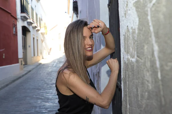 stock image Young blonde woman dressed in black t-shirt and jeans leaning against an old wall. The woman is happy and smiling. Yellow day concept.