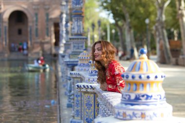 Güzel bir genç kadın geleneksel bir Fas kırmızı elbisesi giyiyor altın ve gümüş işlemeli. Güzel kadın Seville 'in Plaza İspanya' sında tipik fayans korkuluklarından aşağıya bakıyor..