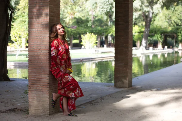 一个漂亮的女人穿着红色的摩洛哥传统服装 绣着金银花 这个漂亮的女人靠在池塘边的柱子上做着不同的表情 — 图库照片