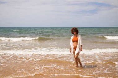Sahilde yürüyen bikinili güzel bir kadın. Kadın farklı jestler ve ifadeler yaparken bir cennet kumsalına yolculuğunun tadını çıkarıyor..