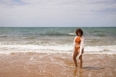 Sahilde yürüyen bikinili güzel bir kadın. Kadın farklı jestler ve ifadeler yaparken bir cennet kumsalına yolculuğunun tadını çıkarıyor..