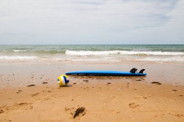 Surfboard and volleyball on the sand of the beach on the shore. In the background you can see the sea. Concept outdoor sports.