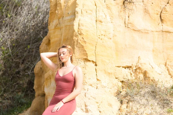 赤い夏のドレスの若い女性が崖の上に立っている 女は身体の表情が違う 背景の岩や植生では — ストック写真