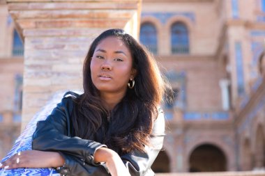 young and beautiful black latin woman visits the most important square in the city of seville. The woman leans her arms on the railing and makes serious and angry expressions.