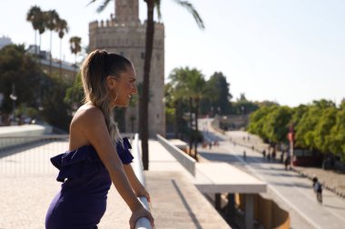Kısa elbiseli genç ve güzel sarışın kadın şehrin geri kalanına tepeden bakan korkuluklara yaslanıyor. Sevilla 'da tatil ve turizm konsepti. İspanya