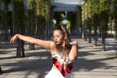 Latin kadın, genç ve güzel dans eden modern dans parktaki sokakta ve farklı ifadeler ve duruşlar sergiliyor. Konsept dansı, hip hop, dans, sanat, aksiyon, güzellik, gençlik sanatı.