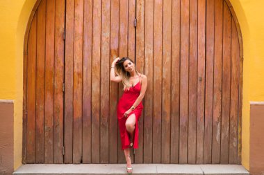 Ahşap bir kapının arka planında kırmızı ipek elbiseli genç ve güzel bir kadın saçına dokunuyor ve değişik yerlere bakarak farklı ifadeler takınıyor. İfadeleri ve jestleri kavra