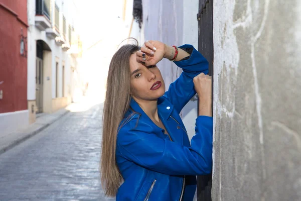 Young blonde woman dressed in blue leather jacket and jeans leaning against an old wall. The woman is sad and depressed and overwhelmed. Concept depression and stress.