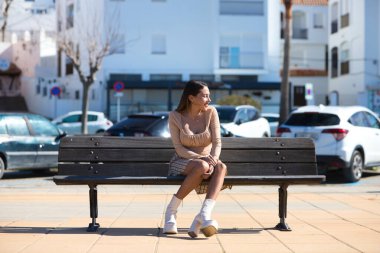 Bankta oturan uzun kahverengi saçlı güzel bir genç kadın. Arka planda Cadiz 'deki Conil kasabasının beyaz sarayları var. Endülüs, İspanya 'da seyahat ve tatil kavramı.