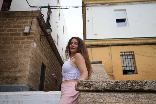 stock image Beautiful blonde woman with curly hair and blue eyes leaning on the wall of the staircase going up to the neighborhood of the city where she is on vacation. Travel concept.