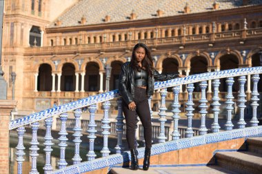 young and beautiful black latin woman is travel in spain and visits the most important square in the city of seville. The woman is dressed in modern and casual black clothes.