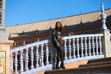young and beautiful black latin woman is travel in spain and visits the most important square in the city of seville. The woman is dressed in modern and casual black clothes.