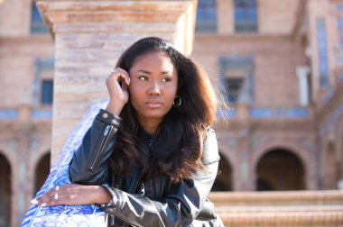 young and beautiful black latin woman visits the most important square in the city of seville. The woman leans her arms on the railing and makes serious and angry expressions.