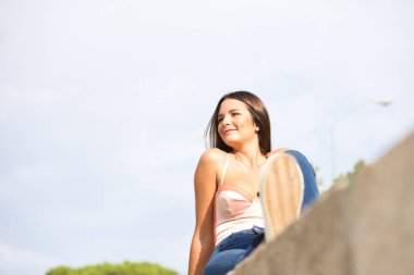 Young beautiful woman sunbathing sitting on a wall. The woman is happy and smiling. Concept of health and well-being.