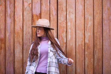 Young and beautiful Spanish woman from Seville with brown hair, hat and checkered shirt standing on a wooden door in different poses and expressions.