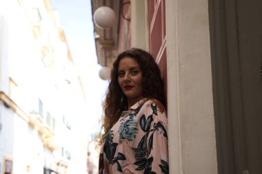 Güzel bir kadın, genç ve sarışın, kıvırcık saçlı ve mavi gözlü sokakta duvara yaslanmış kameraya şehvetli bir şekilde bakan fotoğraflar için poz veriyor. Kadın İspanya, Avrupa 'da tatilde..