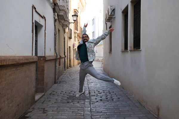 stock image A handsome young man with a beard and glasses is jumping for joy in a narrow street. Happiness and joy concept.