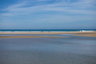 Cadiz, Endülüs ve İspanya 'daki Conil kasabasının panoramik manzarası. Gökyüzü açık ve mavi, beyaz bulutlar var. Deniz kıyısında yürüyen ve gezinen insanlar var..