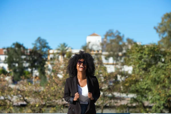 Young beautiful black woman with afro hair dressed in casual clothes is in seville, spain. The woman is happy and smiling. In the background the river and part of the city. Travel and holiday concept