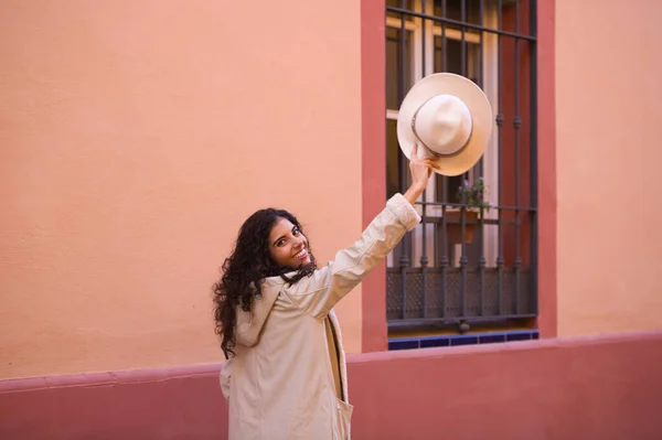 곱슬머리의 아름다운 스페인 머리의 여자가 여행을 즐기면서 손으로 모자를 — 스톡 사진