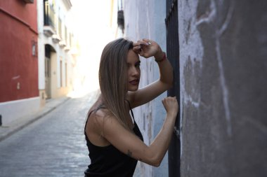 Young blonde woman dressed in black t-shirt and jeans leaning against an old wall. The woman is sad and depressed and overwhelmed. Concept depression and stress.