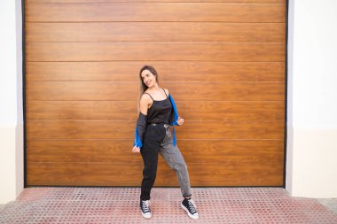 young and beautiful blonde woman dressed in black t-shirt and blue leather jacket and jeans on wooden background poses for photos doing different poses like a model. Beauty and fashion concept.