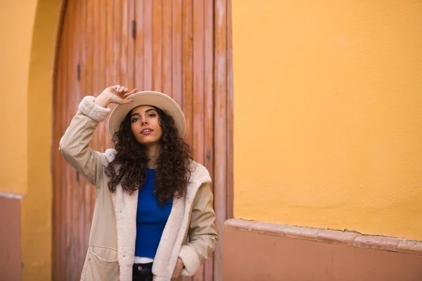 年轻而美丽的西班牙黑发女人 卷曲的头发 头戴帽子 身穿外套 走在塞维尔市寒冷的街道上 一边做着不同的表情 一边玩乐 — 图库照片
