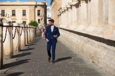 Sakallı, mavi takım elbiseli ve kravatlı yakışıklı genç adam İspanya 'daki Sevilla katedralinin yanından geçiyor. Bu adam şehirde bir iş gezisinde olan bir yönetici.