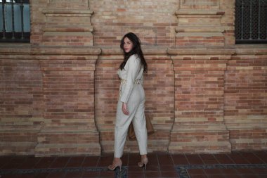 Uzun kahverengi saçlı genç ve güzel kadın Sevilla 'nın en ünlü meydanında. Kadın kırmızı tuğlalardan oluşan bir arka planda farklı duruş ve vücut ifadeleri sergiliyor.